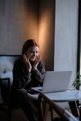 red-haired woman freelancer works remotely on laptop in cafe.
