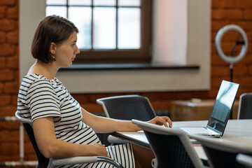 Pregnant woman sitting at desk with computer in office. Real person in real situation.