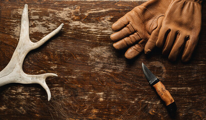 Reindeer antlers, leather gloves and a hunting knife on a rustic wooden table  - top view