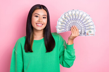 Photo of good mood cute girl dressed green sweatshirt rising dollars fan isolated pink color background