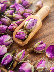 Gently pink dried rose buds close-up in and around a tea scoop. Selective focus. Wooden table. Vertical.