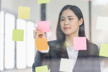 Business female employee with many conflicting priorities arranging sticky notes commenting and...