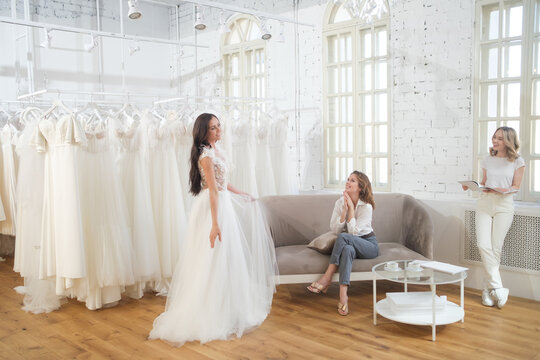 Woman trying on wedding dress with female friends having fun and taking photographs.