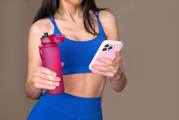 Fit  woman holding water bottle and mobile phone . Fitness woman drinking water during  workout...