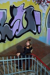 A woman in leather clothes stands in the entrance against the background of a wall with graffiti