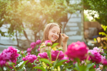 Obraz na płótnie Canvas Happy little girl with braces in the garden in bushes of peonies