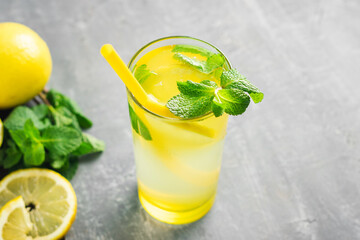 Lemonade drink or mojito cocktail in a glass with straw, lemon fruit and mint leaves, refreshing summer beverage