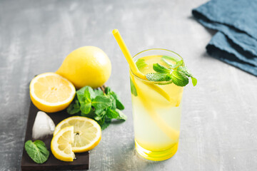 Lemonade drink or mojito cocktail in a glass with straw, lemon fruit and mint leaves, refreshing summer beverage