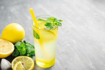 Lemonade drink or mojito cocktail in a glass with straw, lemon fruit and mint leaves, refreshing summer beverage