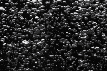 A lot of shiny air bubbles of different sizes underwater on a black isolated background. Close up of light lit oxygen bubbles flow upwards. Aeration or filtration of liquid. Fizzy flow of air bubbles.