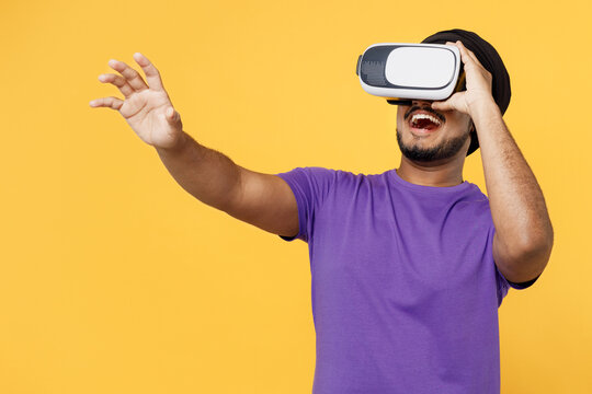 Devotee Sikh Indian man ties his traditional turban dastar wear purple t-shirt watch in vr headset pc gadget stretch hand isolated on plain yellow background studio portrait. People lifestyle concept. - Powered by Adobe
