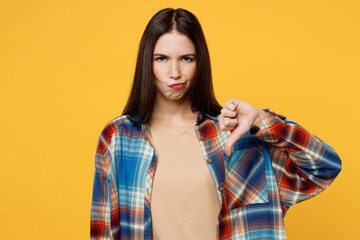Young sad mad dissatisfied displeased caucasian woman wearing blue shirt beige t-shirt showing thumb down dislike gesture isolated on plain yellow background studio portrait. People lifestyle concept.