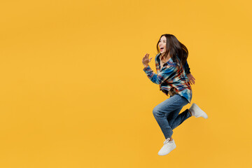 Fototapeta na wymiar Full body side view young smiling excited caucasian fun woman wear blue shirt beige t-shirt jump high run fast hurry up isolated on plain yellow background studio portrait. People lifestyle concept.