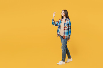 Fototapeta na wymiar Full body side view young smiling cheerful caucasian woman wears blue shirt beige t-shirt walk go strolling waving hand isolated on plain yellow background studio portrait. People lifestyle concept.