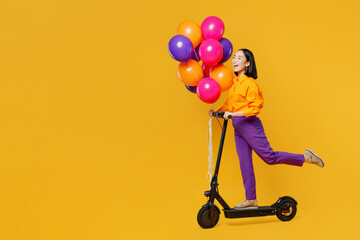 Full body sideways happy fun young woman wearing casual clothes hat celebrating hold bunch of balloons riding e-roller scooter isolated on plain yellow background. Birthday 8 14 holiday party concept. © ViDi Studio