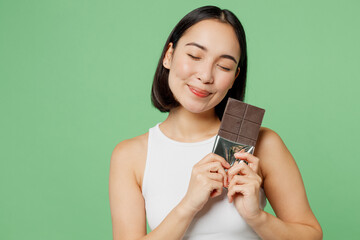 Young satisfied happy woman wear white clothes hold in hand dark chocolate bar close eyes isolated...