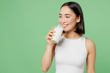 Young smiling happy fun woman wear white clothes hold in hand glass drink milk look aside isolated on plain pastel light green background. Proper nutrition healthy fast food unhealthy choice concept. © ViDi Studio