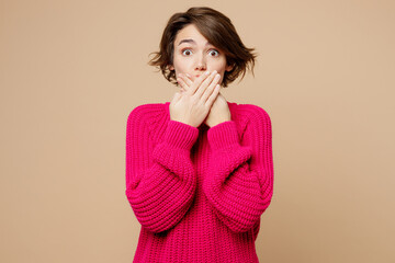 Young sad surprised scared frightened fearful caucasian woman she wearing pink sweater cover mouth with hand isolated on plain pastel light beige background studio portrait. People lifestyle concept.