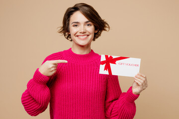 Young fun smiling woman wear pink sweater hold point finger on gift certificate coupon voucher card...