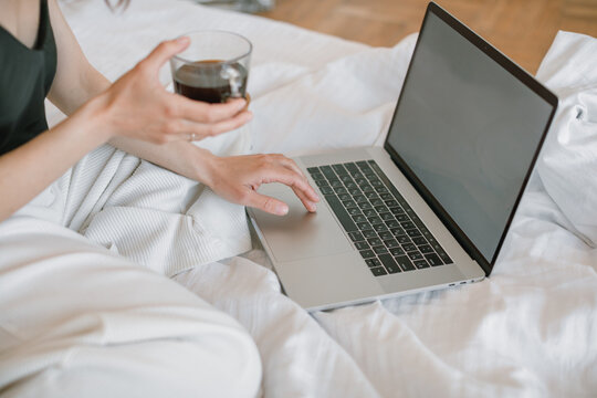 Woman Sitting On Her Bed In Front Of A Laptop Computer Drinking A Cup Of Coffee