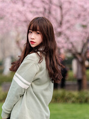 Outdoor portrait of beautiful young Chinese girl in Japanese JK style dress posing with blossom cherry tree brunch background in spring garden, beauty, summer, emotion, expression and people concept.