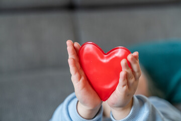 A toddler girl is holding two red hearts