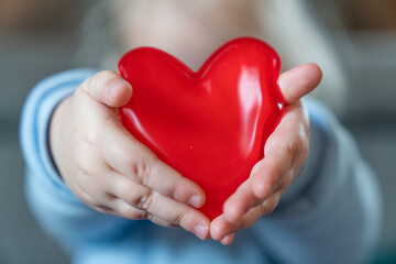 A toddler girl is holding two red hearts