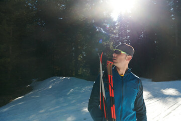 Portrait handsome male athlete with cross country skis in hands and goggles, training in snowy...