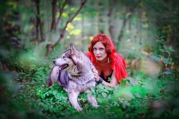 Red-haired beautiful girl in the forest. Girl from a fairy tale. Girl in a black corset. Redhead. Outdoors. Girl in a red cape. Girl in a red coat. Summer. Little Red Riding Hood. Girl with a wolf in