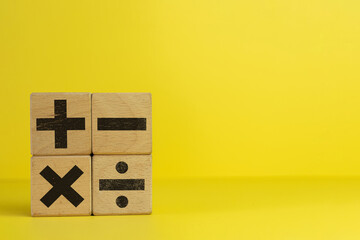 Image of wooden cubes displaying mathematical operation icons of Plus, minus, multiply and divide on a yellow background in left side photo with copyspace use for education,mathematic,symbol concept.