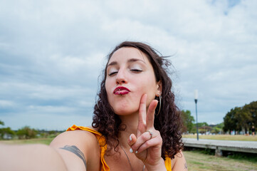 selfie of young latin woman looking at the camera giving a kiss and making peace and love sign