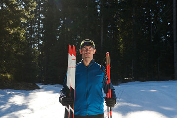 Portrait handsome male athlete with cross country skis in hands and goggles, training in snowy...