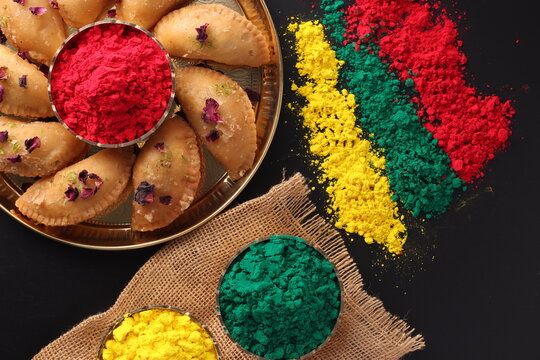 Holi Indian festival of colors celebrating with colorful Gulal Abeer mawa gujia mithai pirukiya sweets presented on a brass plate and scattered isolated on black background