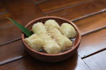 a close up of sticky rice with grated coconut and brown sugar sauce served in a wooden bowl. Indonesian traditional food photo concept. In Indonesia it is called lupis.
