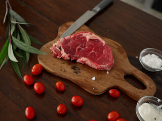 Composition of raw steak meat on a kitchen wooden table with spices, salt, vegetables and herbs, cooking, top view, copy place for recipes.