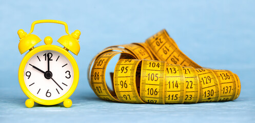 Yellow retro alarm clock and tape measure on blue background, weight loss, diet banner
