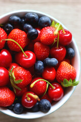 Bowl filled with fresh blueberries, cherries and strawberries on wooden table. Top view.