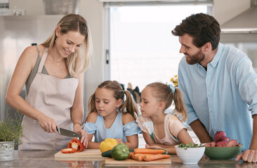 Mom, dad and children cooking in kitchen with vegetables for nutrition, healthy lunch and vegan diet. Family, food and parents with girls learning, teaching and helping cut ingredients for meal prep