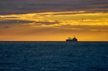 Silhouette of a fishing ship on the horizon of the sea against the backdrop of a dramatic sunset with sunbeams