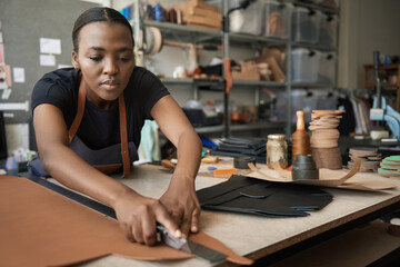 Young African female leather worker cutting leather at a bench