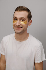 Gorgeous happy smiled young man with patches under eyes. Beauty routine, cosmetic concept