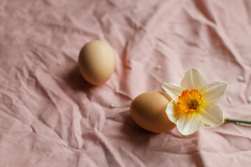 Fototapeta na wymiar Natural eggs and blooming daffodil flower on pink fabric background. Happy Easter! Rustic easter still life. Space for text