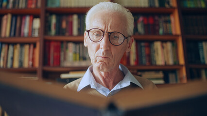 Senior male researcher in eyeglasses reading an interesting book, wisdom