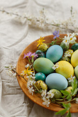 Rustic easter still life. Stylish easter eggs and blooming spring flowers in wooden bowl on linen fabric. Happy Easter! Natural painted eggs and blossoms on rural table
