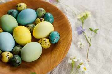 Obraz na płótnie Canvas Happy Easter! Stylish easter eggs and blooming spring flowers in wooden bowl on rustic table. Natural painted eggs and blossoms on linen fabric. Rustic easter still life