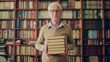 Portrait of smiling senior librarian holding a stack of books, knowledge, wisdom