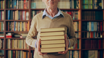 Mature man writer holding in hands a series of his bestseller books, meeting fans at the library