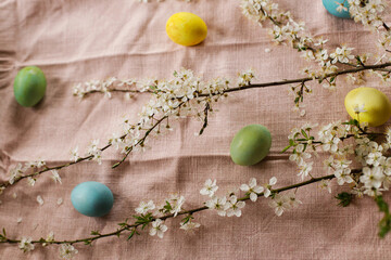 Stylish easter eggs and blooming cherry flowers on rustic table. Happy Easter! Rustic easter still life. Natural painted eggs and cherry blossoms on pink linen fabric