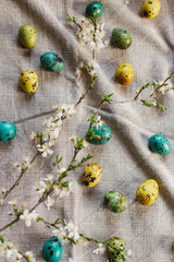 Happy Easter! Stylish easter eggs and blooming cherry branch on rustic table. Rustic easter flat lay. Natural painted quail eggs and spring blossom on linen fabric
