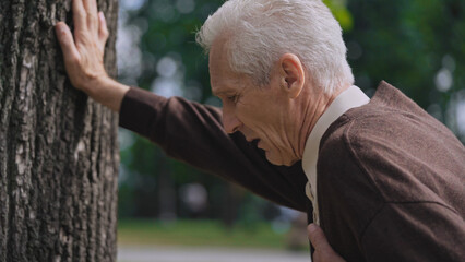 Sad mature male suffering heart attack, leaning on tree, person in need of help